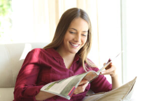 Happy woman reading a magazine sitting on a sofa in the living room at home