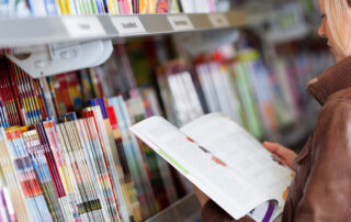 Woman reading a magazine which she has just removed for a display on a shelf in a supermarket